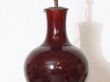 un vase rouge posé sur une étagère blanche à côté d'une lampe