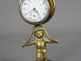 une horloge en or posée sur un socle, sur lequel se trouve un petit garçon