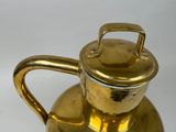 a gold tea pot with a handle on a white table