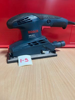 La ponceuse orbitale Bosch est posée sur une table, à côté d'une boîte rouge