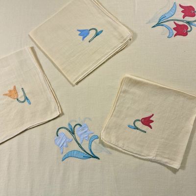 four napkins with embroidered flowers on them on a table