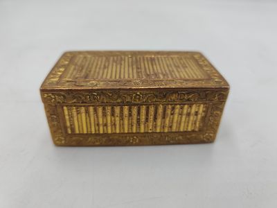 une petite boîte en or avec un couvercle en bois, posée sur une surface blanche