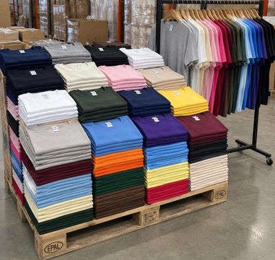 de nombreux t-shirts de différentes couleurs empilés sur une palette dans un magasin