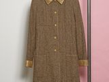 un manteau en tweed marron, avec un col et des poignets dorés, suspendu à un cintre devant un mur rose
