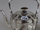 a silver tea pot and two spoons on a table