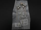 trois épingles en argent ornées de perles sont posées sur un morceau de papier