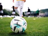 un ballon de foot posé sur l'herbe devant un footballeur