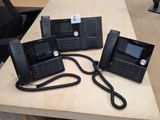 trois téléphones noirs posés les uns à côté des autres sur un bureau en bois
