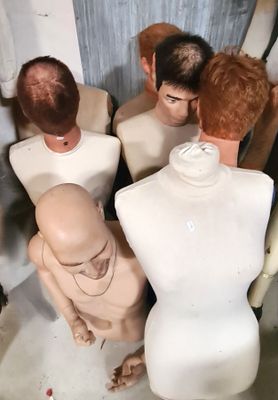 Plusieurs mannequins sont alignés dans une pièce aux murs blancs