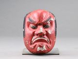 un masque rouge posé sur un socle, sur fond gris