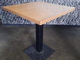 square wooden table with black metal base in front of a patterned wall