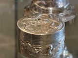 une boîte en argent ornée d'un dragon, posée sur une étagère en verre