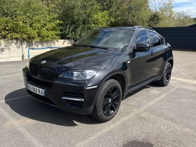La BMW X6 est garée sur un parking, avec des arbres en arrière-plan.