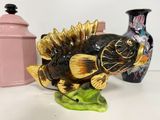 yellow and black fish figurine sitting on top of a green leaf next to a pink vase