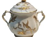 a white and gold vase with a lid and a bird on it