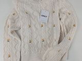 Le pull est blanc et orné de boutons dorés.