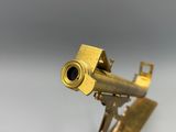 un petit télescope en laiton posé sur un support, sur une surface blanche