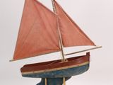 a small wooden boat with a red sail on a stand