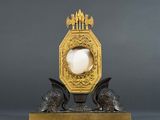 a gold clock on a stand with a white egg in it