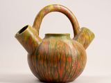 an orange and green teapot with a handle on a white surface