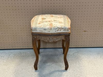 un petit tabouret dont l'assise est recouverte d'un tissu à motifs floraux