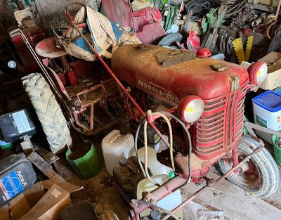un vieux tracteur rouge dans un garage où se trouvent de nombreux autres objets