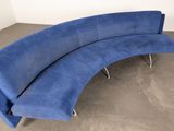 a blue curved couch in a room with concrete flooring
