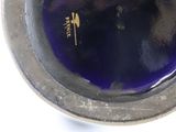 a blue glass in a silver bowl on a white surface