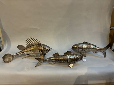 trois poissons en métal posés sur une table blanche, à côté d'une chaise