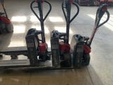 Trois diables électriques sont alignés sur une palette dans un entrepôt