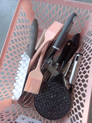 un panier rose rempli d'ustensiles de cuisine et de tampons à récurer