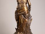 an antique bronze statue of a woman sitting on a tree stump