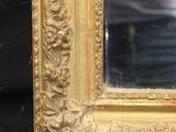 a gold framed mirror on a black table with a person in the background