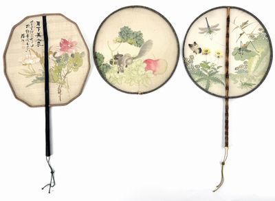 three chinese fan with designs of flowers and birds hanging on a wall