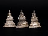 trois figurines en argent représentant des bouddhas assis sur une table