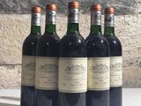six bouteilles de vin sont alignées sur une table devant un mur de pierre