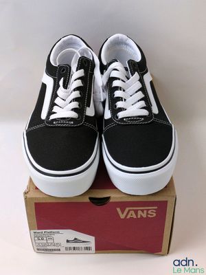 une paire de baskets Vans noires et blanches posées sur une boîte