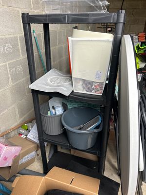 a black shelf with a white refrigerator and a black trash can in it