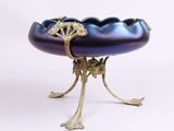 un bol violet posé sur un socle doré, sur fond blanc