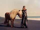 a woman that is standing next to a horse on the beach