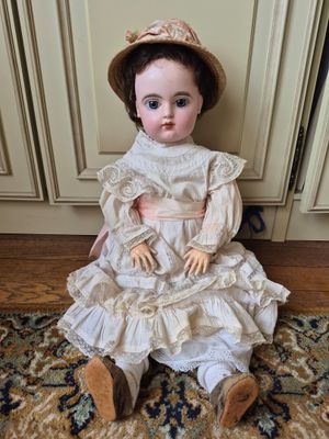 doll sitting on a rug in front of a door wearing a hat and dress