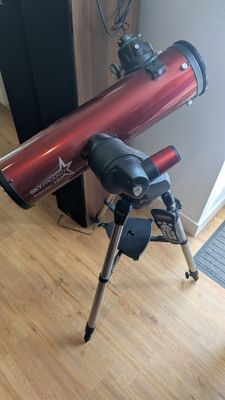 un télescope posé sur un trépied, sur un plancher en bois