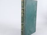 an old book with a green cover sitting on a white surface