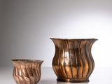pair of bronze vases on a white table with a white background