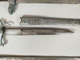 three silver metal swords are displayed on a white surface