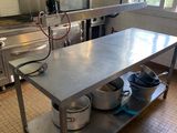 une grande table en acier inoxydable sur laquelle sont posés des casseroles et des poêles