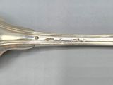 an antique silverware spoon with a long handle on a gray surface