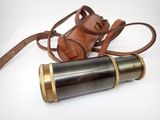 un vieux télescope avec un étui en cuir et une lanière, posé sur une surface blanche