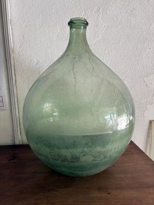 a green glass vase sitting on a table next to a white wall