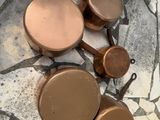 quatre casseroles et poêles en cuivre posées sur un sol en marbre